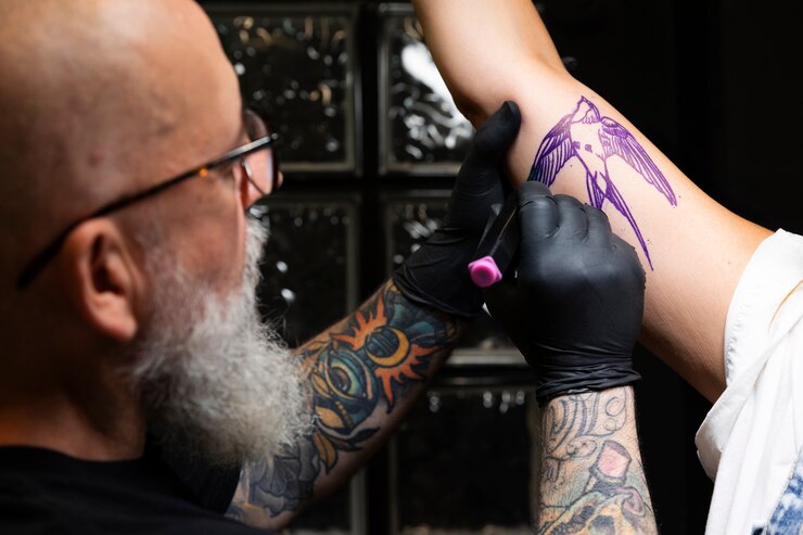 A tattoo artist is drawing a bird on another man's hand.