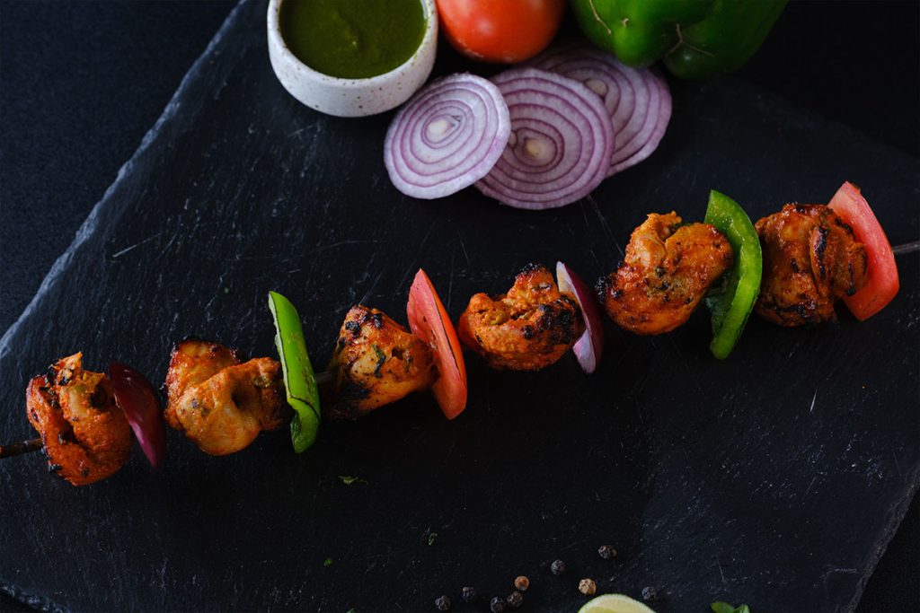 Murgh Tikka Kebab with mint sauce and red onion slices on a black plate at Queens of India Kuta Bali